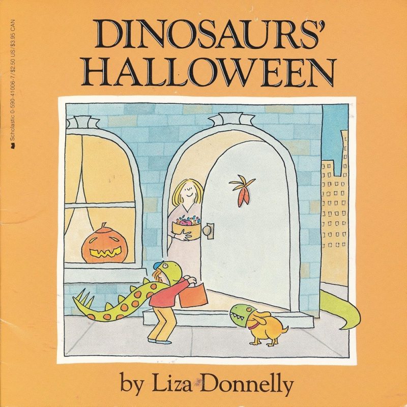 Boy dressed up a Dinosaurs for Halloween standing by an open door to a home holding a candy bucket.